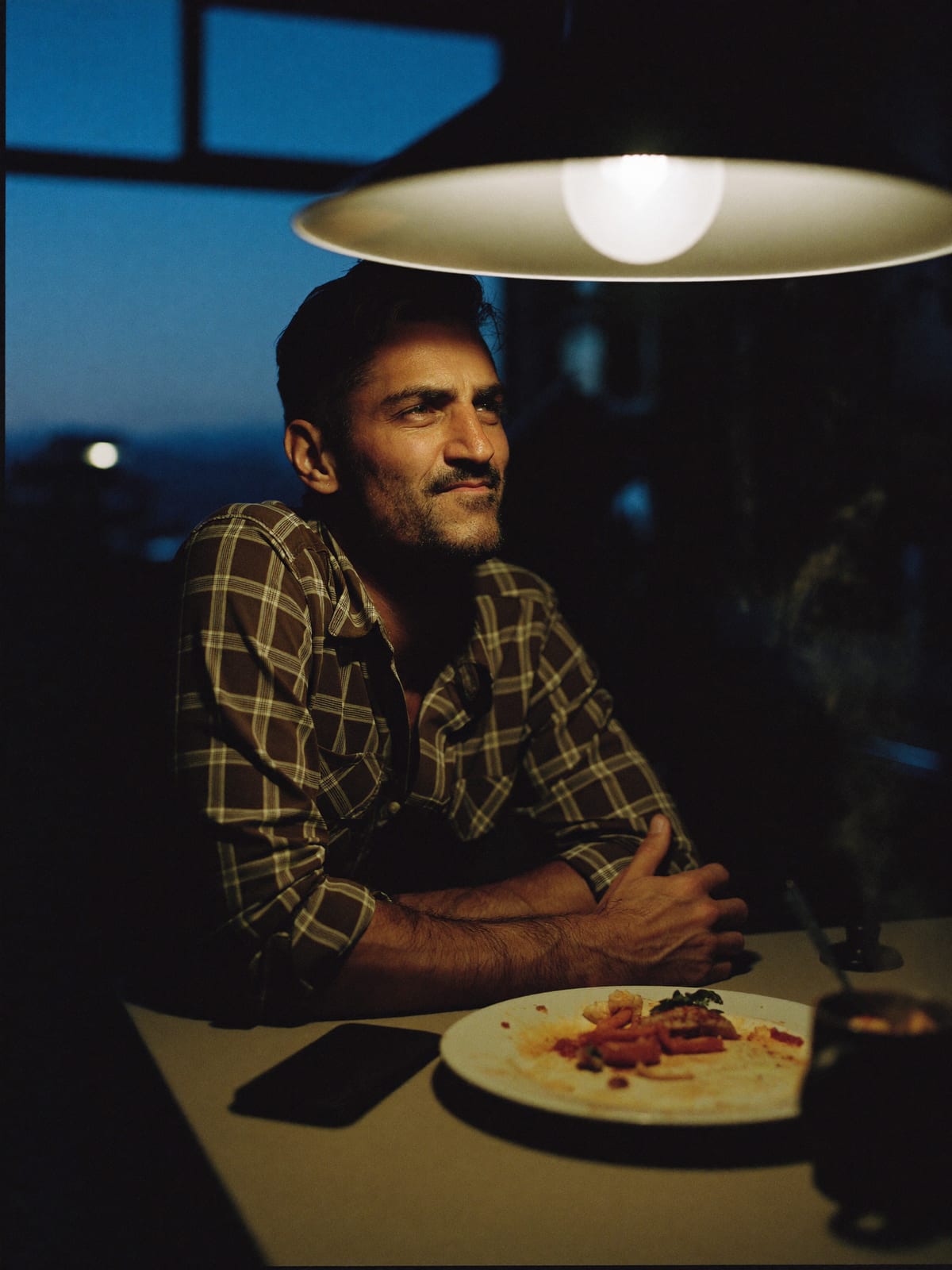 A business owner relaxed at his kitchen table at dusk, phone face-down beside his plate